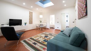 A living room with a flat-screen TV, a blue sofa, a patterned rug, and a skylight.
