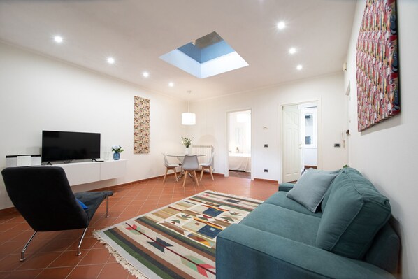 A living room with a flat-screen TV, a blue sofa, a patterned rug, and a skylight.