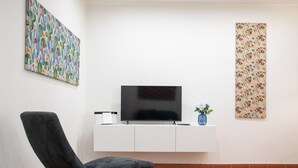 A modern living room with a flat-screen TV on a white cabinet, a black armchair, and two pieces of wall art.