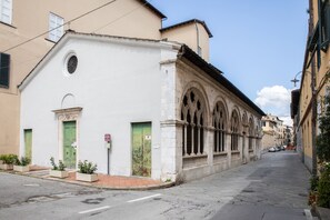 Une rue étroite bordée d’un immeuble à la façade blanche, aux portes vertes et aux fenêtres en arc de cercle.