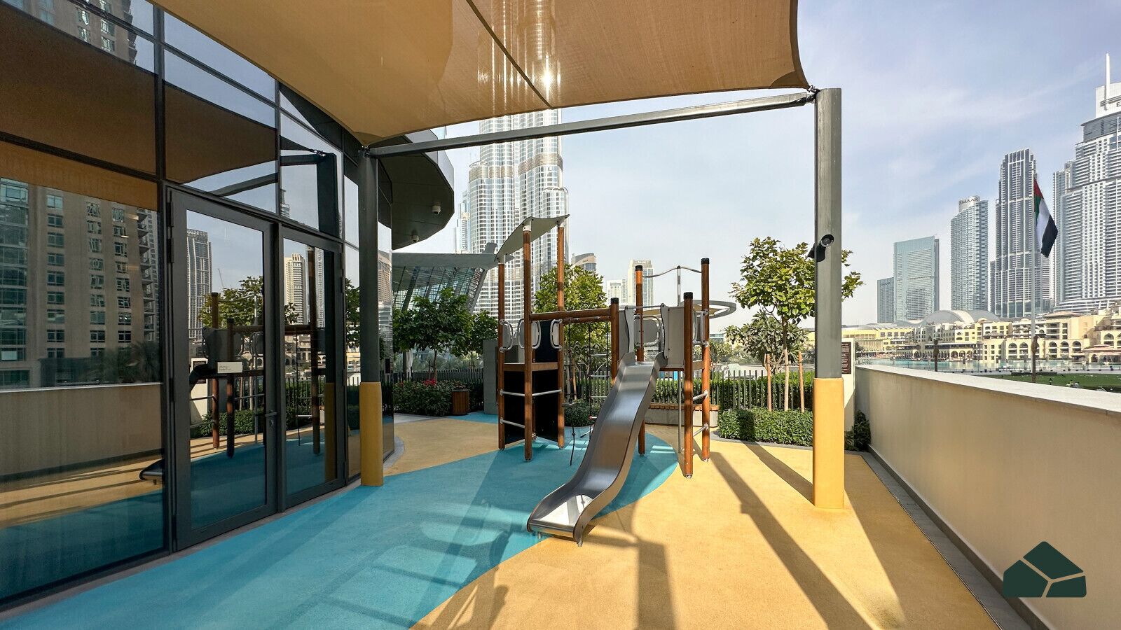 Een dakterras met een speeltuin, een glijbaan en klimconstructies, omgeven door glazen wanden met uitzicht op de stad.