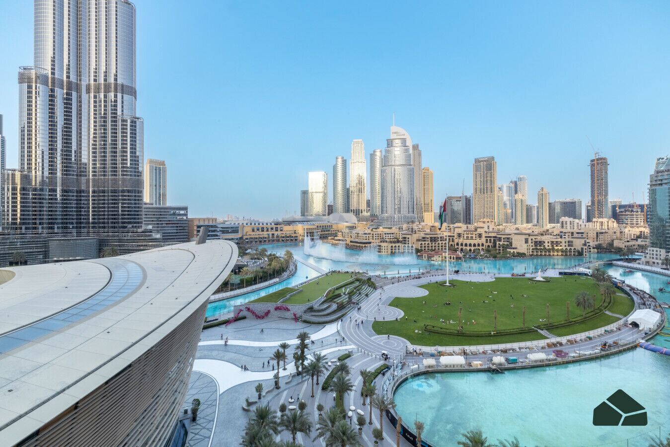 A cityscape with modern high-rise buildings, a large central fountain, and a well-maintained park area.