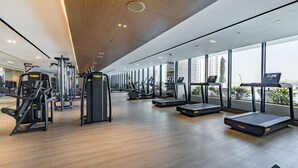 A modern gym with various exercise equipment, large windows, and a view of the city. - Canal View Studio | Private Jacuzzi | BMS (Dubai)