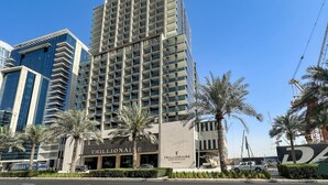 A high-rise building with balconies, a sign reading "TRILLIONAIRE," and palm trees in the foreground. - Canal View Studio | Private Jacuzzi | BMS (Dubai)