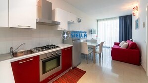 Une cuisine moderne avec des meubles blancs, un plan de travail rouge et un coin repas comprenant un canapé rouge et une table blanche.