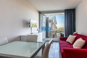 A modern hotel room with a glass dining table, a red sofa, a TV on the wall, and a balcony with a city view. - / Magnolie / ° Eraclea Mare Apt ° (Eraclea Mare)
