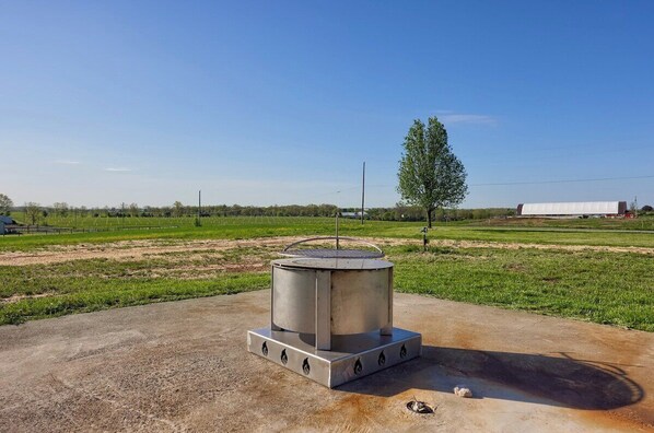 A concrete outdoor area with a cylindrical structure, a tree, and a distant building.
