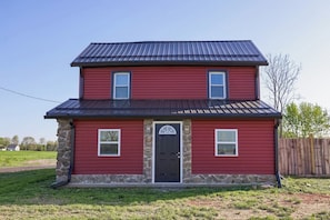 A two-story house with a red exterior, stone foundation, and a black roof. - Homestead Haven | Fire Pit, Pickleball & Fun (Gettysburg)