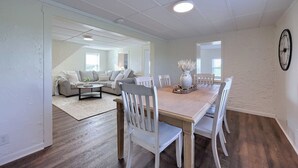 Een ruime woonkamer met een eettafel, witte stoelen, een zithoek en een grote klok aan de muur.