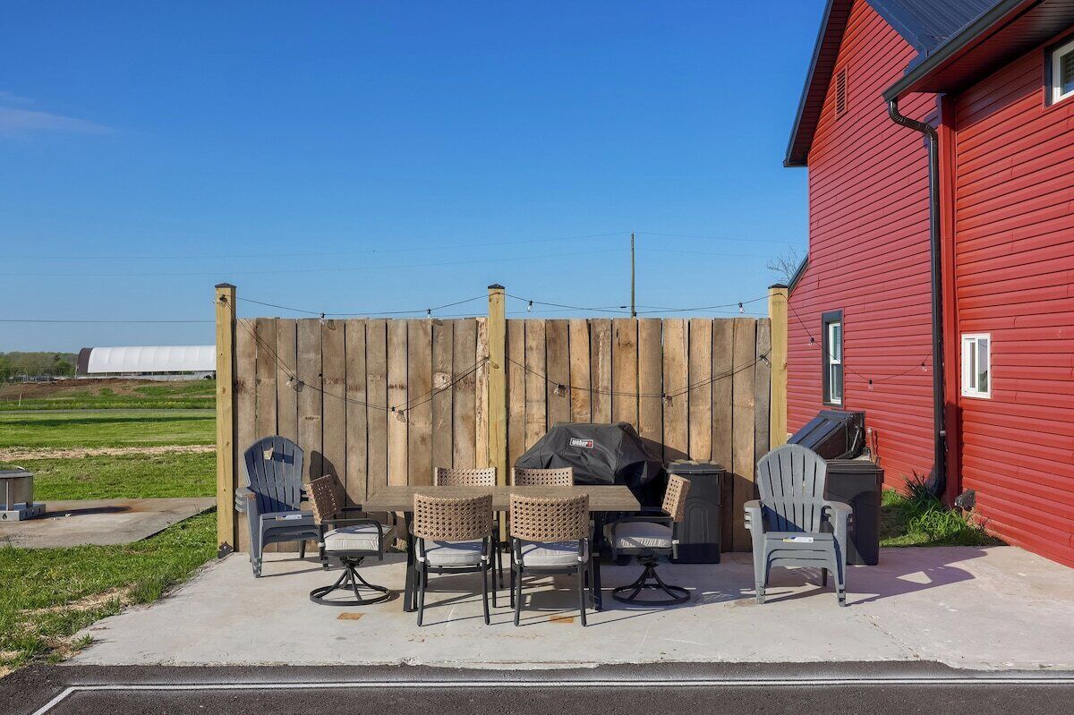Et rødt hus med et træhegn, udendørs siddepladser med stole og et bord, samt en grill.