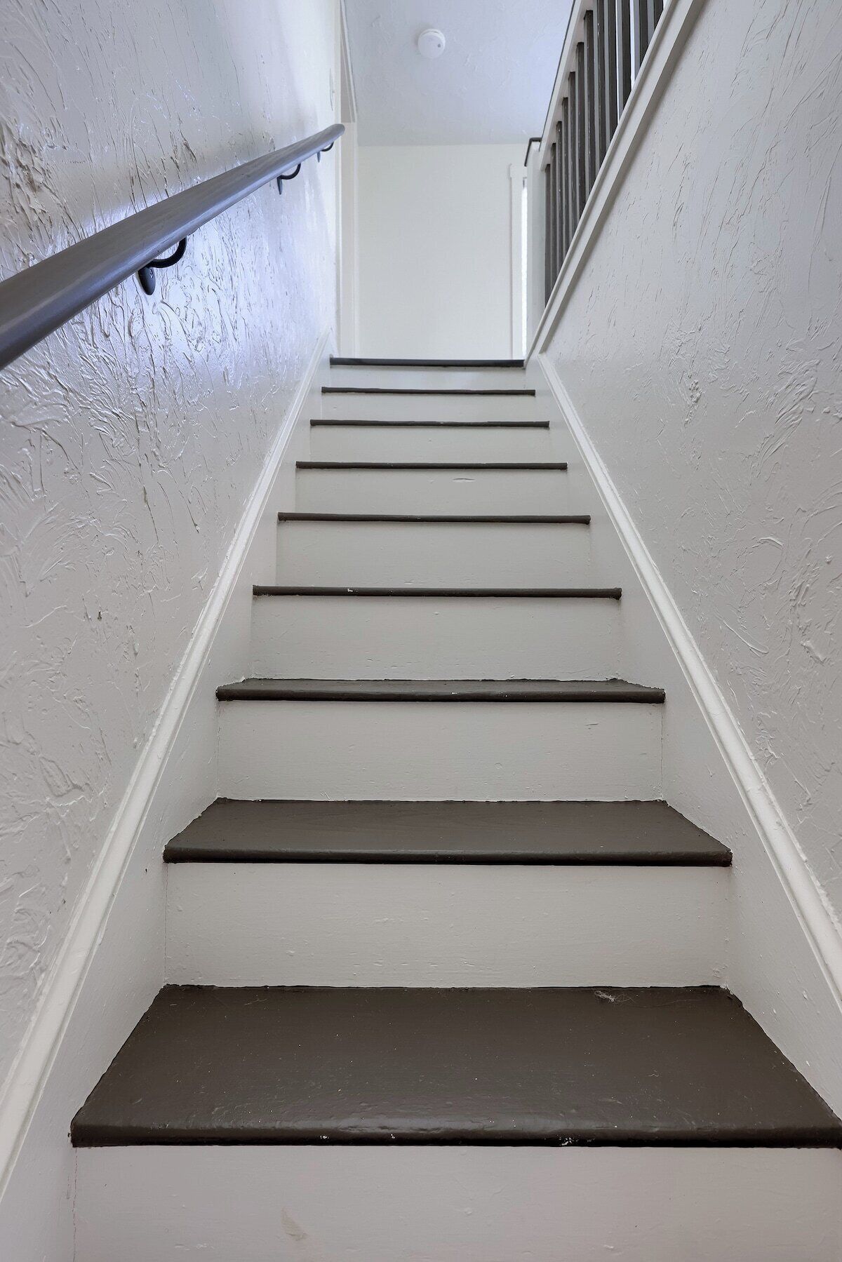 A staircase with white walls and dark steps leading upwards.