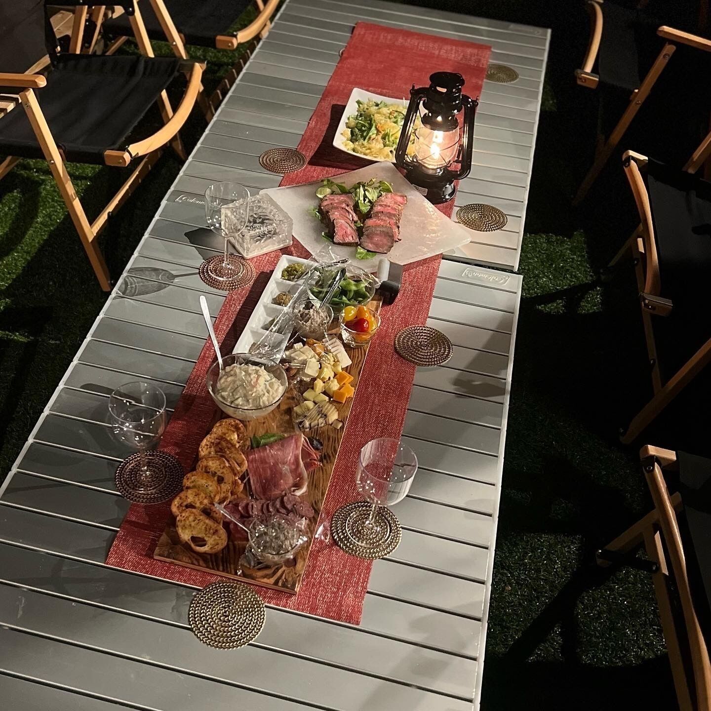 Una larga mesa de comedor con un camino de mesa rojo, dispuesta con distintos platos, copas y un farol.