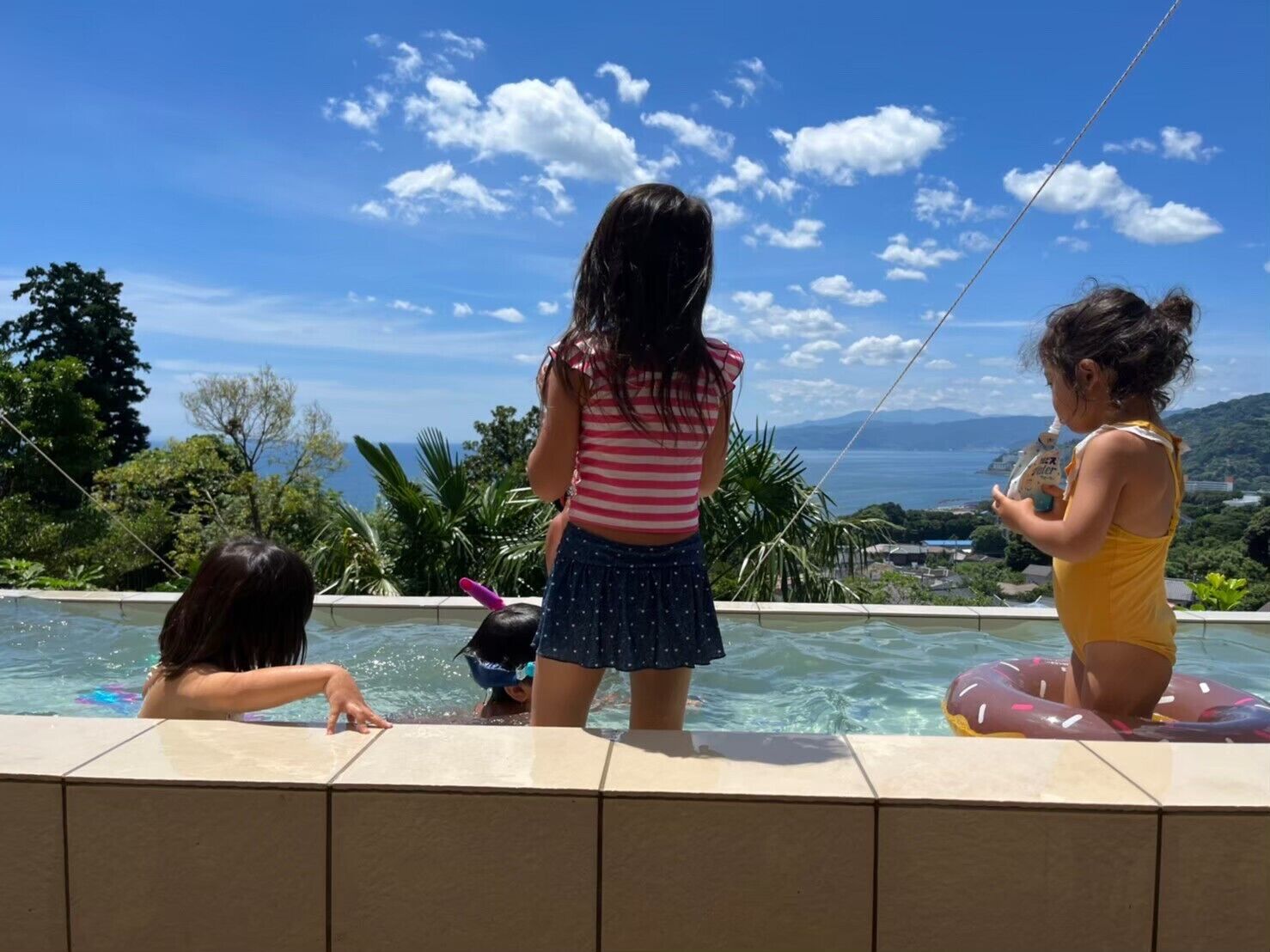 Un espace aménagé au bord de la piscine offrant une vue dégagée sur l’océan et le paysage lointain.
