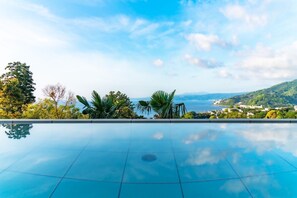 Une piscine d’un bleu éclatant, avec vue sur la mer et les collines en arrière-plan.