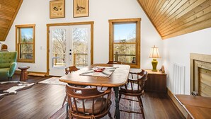 A dining area with a wooden table and chairs, large windows, and a fireplace. - Modern A-Frame Away from it All! (Marshall)