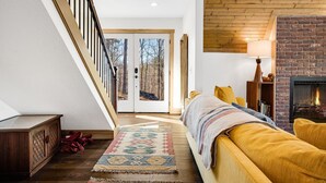 A cozy living room with a staircase, a fireplace, and a view of the outdoors. - Modern A-Frame Away from it All! (Marshall)