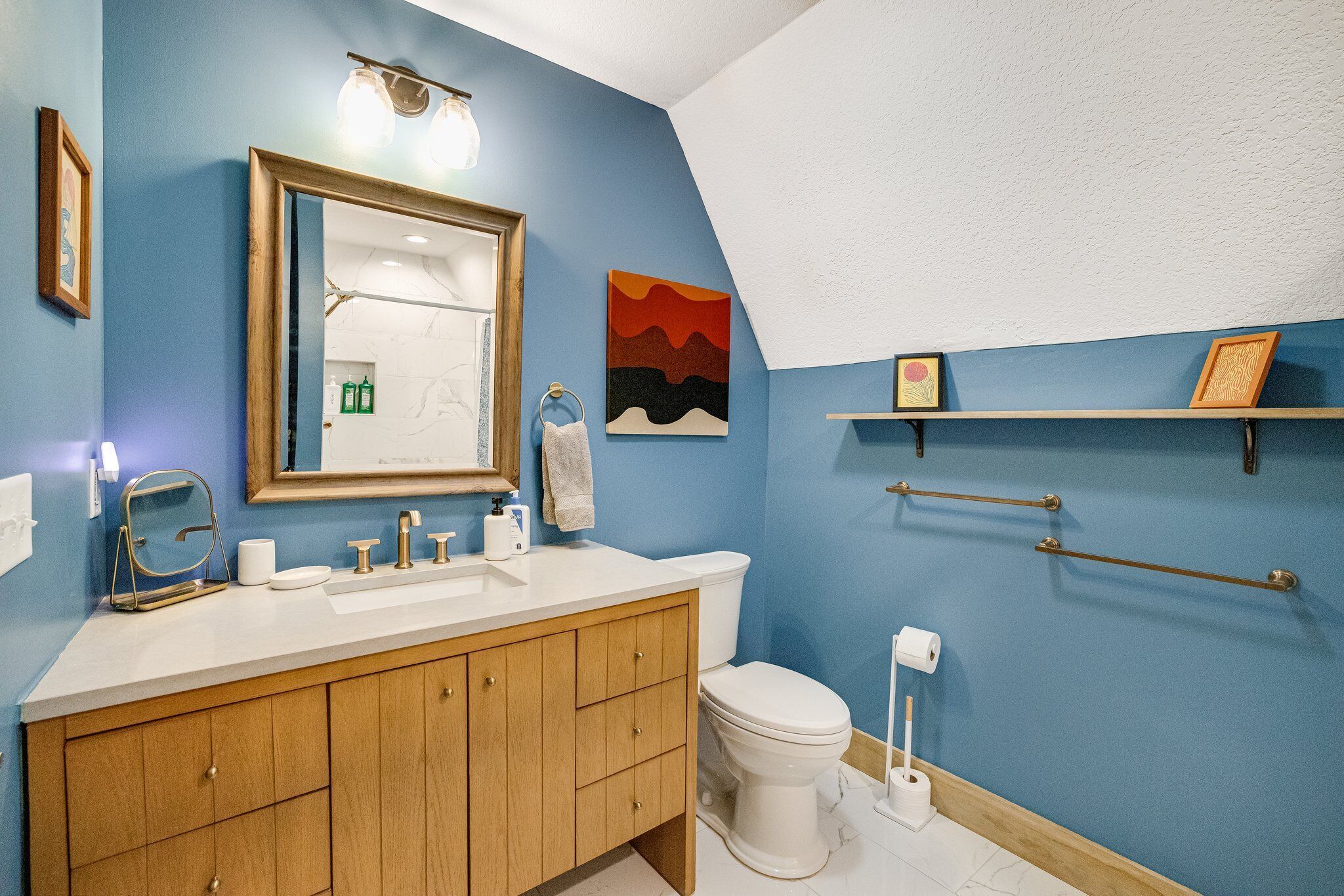 Ein Badezimmer mit blauer Wand, Waschtisch aus Holz, weißem Waschbecken und Toilette.