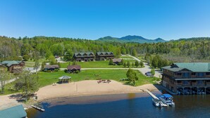 A lakeside lodge with multiple buildings, a sandy beach, and a dock with boats.