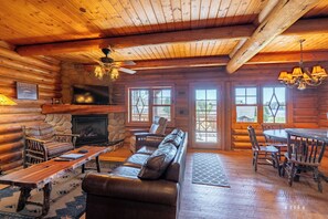 Cozy cabin interior with a stone fireplace, leather sofa, and dining area.