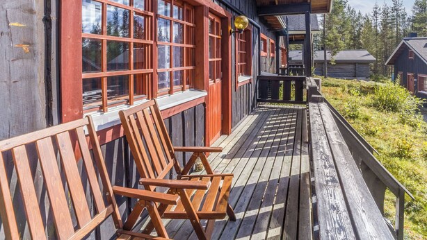 Eine Holzhütte mit Veranda, Holzstühlen und Blick auf den umliegenden Wald.