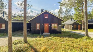 Eine rustikale Holzhütte mit roter Tür, umgeben von hohen Bäumen und einer Rasenfläche.