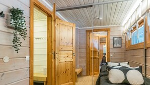 Una habitación cálida de cabaña de madera con una cama, un banco y una puerta que da al baño.