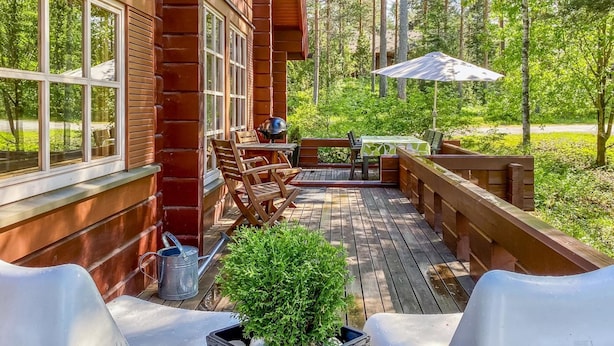 Una terraza de madera con mobiliario exterior, una parrilla y una planta en maceta.