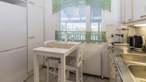 A compact kitchen with white cabinets, a small dining table, and a window with lace curtains.