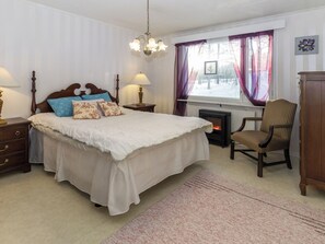 Un dormitorio con una cama grande, lámparas de noche, una silla, una chimenea y una ventana con cortinas.