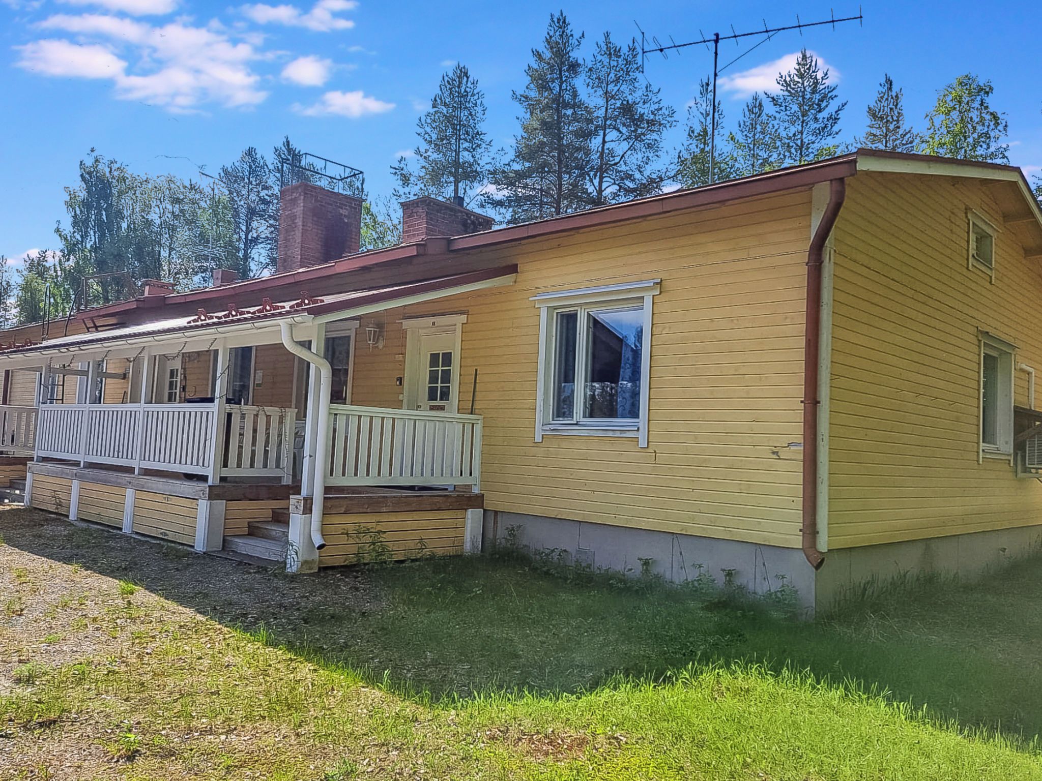 A yellow wooden house with a porch and a chimney.