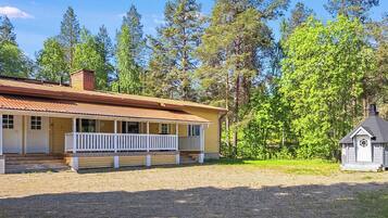 A single-story house with a porch, a small shed, and a forested background.