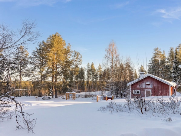 A snow-covered landscape with a red cabin, a wooden bench, and a snow-covered path.