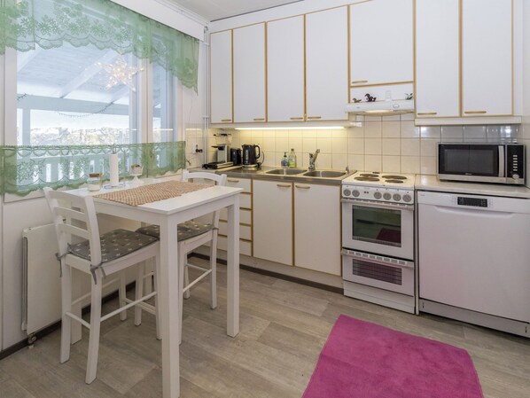 Una cocina con alacenas blancas, estufa, microondas y una mesa de comedor con sillas.