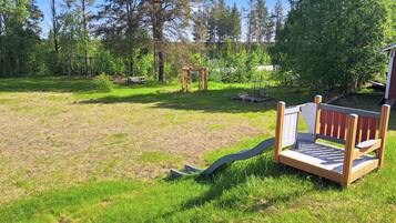 A grassy outdoor area with a wooden bench, a swing set, and a small wooden structure.