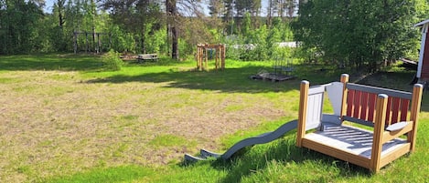 A grassy outdoor area with a wooden bench, a swing set, and a small wooden structure.