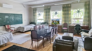 A dormitory room with bunk beds, a dining table, chairs, a desk, and a television.