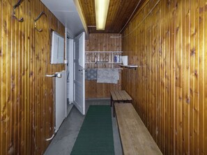 Un pasillo estrecho con paredes de madera, un banco, una pequeña mesa y una puerta que da a otra habitación.