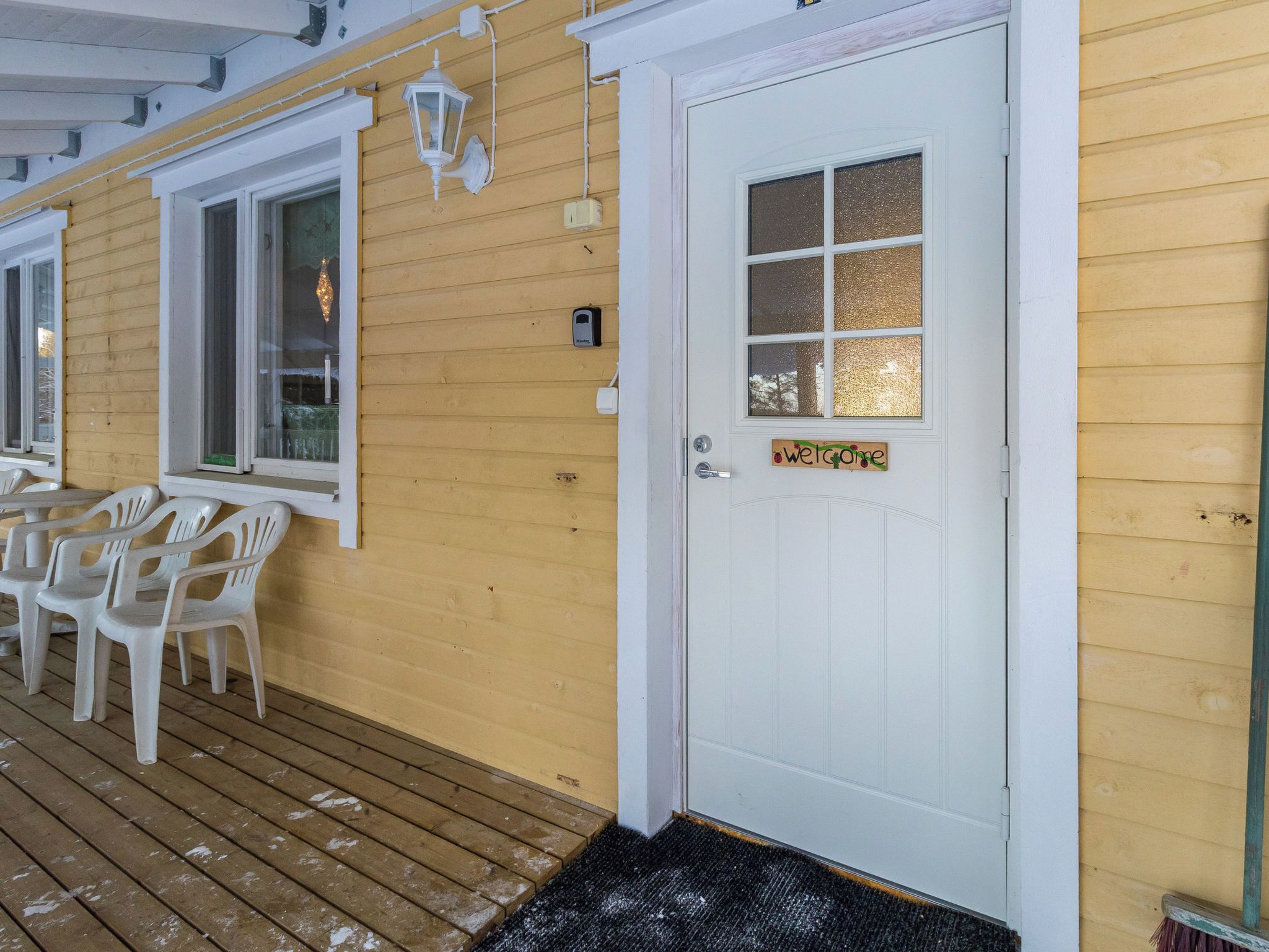 A wooden exterior with a white door, a window with a 'Welcome' sign, and outdoor seating with chairs.