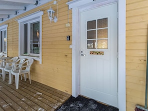 A wooden exterior with a white door, a window with a 'Welcome' sign, and outdoor seating with chairs.