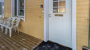 A wooden deck with white plastic chairs, a white door with a window, and a welcome sign.