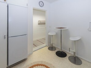 A compact kitchen with a white refrigerator, a clock on the wall, and two bar stools. - Kelloselkä b by Interhome (Salla)