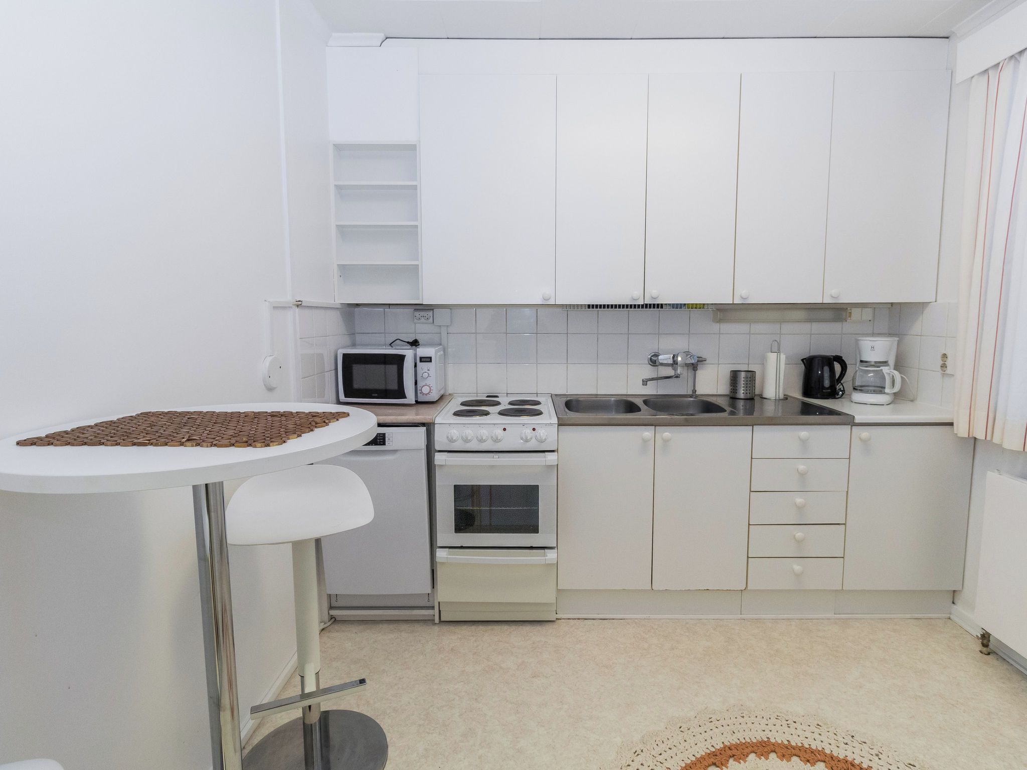 Cocina compacta con armarios blancos, microondas, estufa y cafetera.