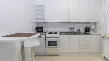Een kleine keuken met witte kastjes, een magnetron, een fornuis en een koffiezetapparaat.