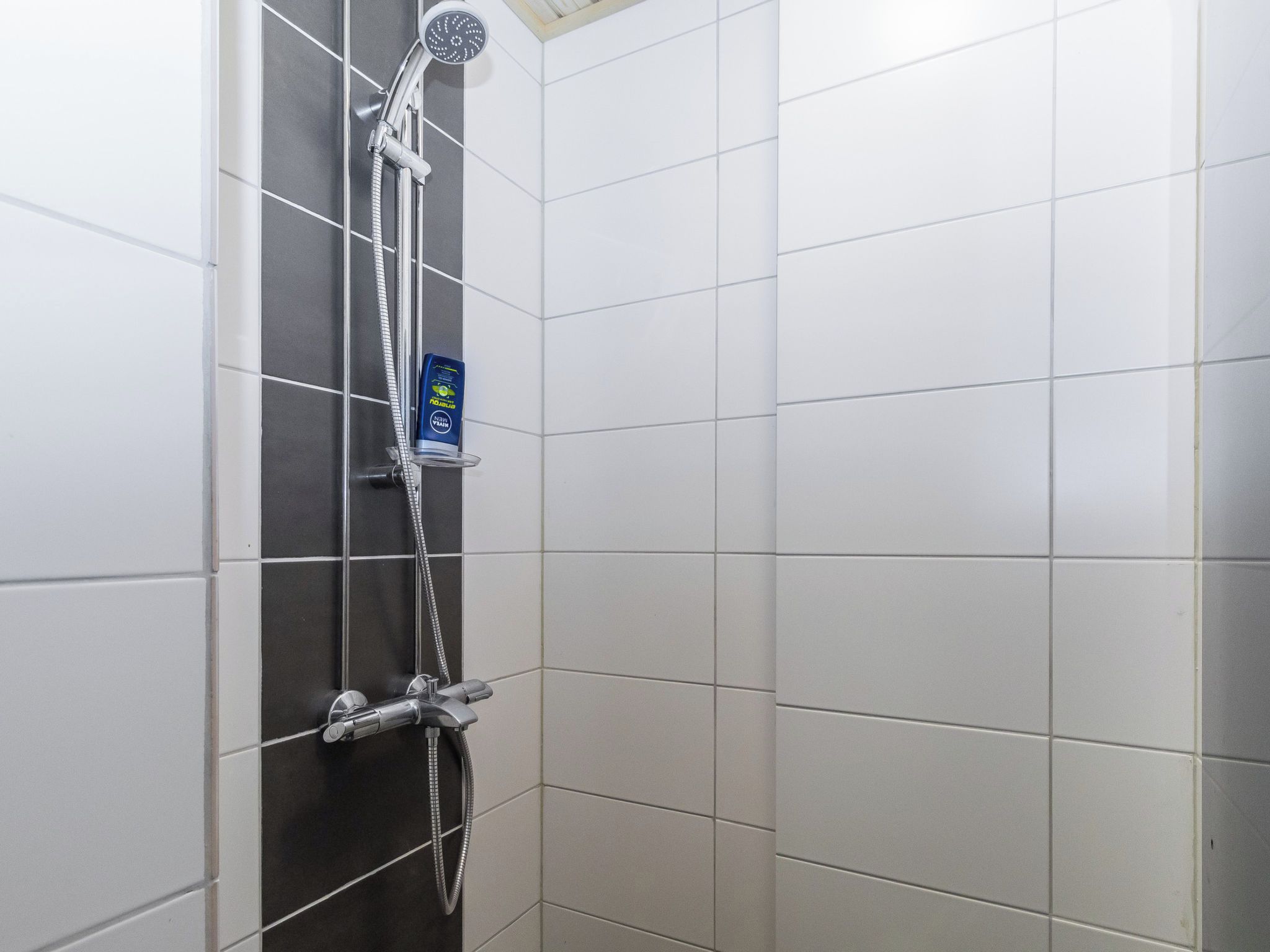 En duschhörna med ett handhållet duschmunstycke, en väggmonterad kontrollpanel och en tvåldispenser.