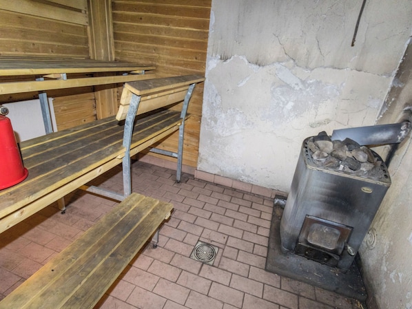 A sauna room with benches, a brick floor, and a wood-burning stove.