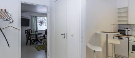 Kompakti keittiö, jossa on mikroaaltouuni, uuni ja pieni ruokailutila tuoleineen ja pöytineen.