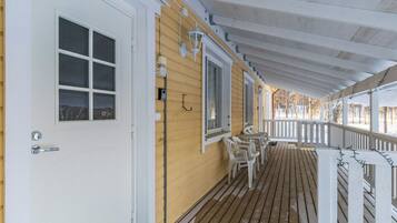 A wooden porch with a white door and windows, outdoor seating, and a railing.