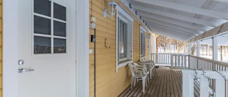 A wooden porch with a white door and windows, outdoor seating, and a railing.