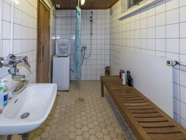 A small bathroom with a sink, a shower, and a bench.