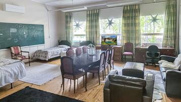 A room with a table, chairs, a bed, a desk, and a television.